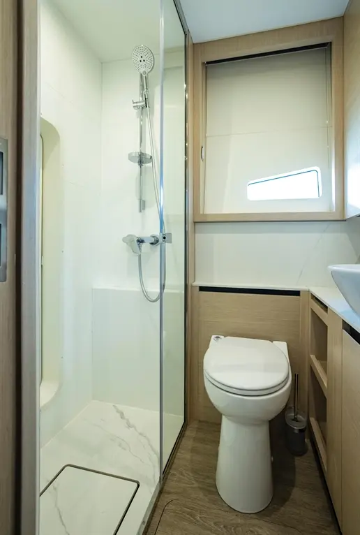 Modern bathroom featuring a glass shower, toilet, and wooden cabinetry with a sleek sink. Natural light from a window.